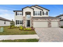 Two-story home with a manicured lawn, brick accents, and a three car garage at 32346 Sapna Chime Dr, Wesley Chapel, FL 33545