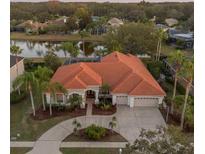 Aerial view of home with red tile roof, a circular driveway, and scenic pond at 3830 Moreno Dr, Palm Harbor, FL 34685