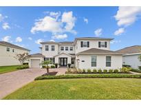 Elegant two-story home showcasing a lush front lawn, charming landscaping, and brick-paved driveway, under a bright sky at 7721 Roma Dune Dr, Wesley Chapel, FL 33545
