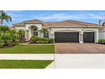 Attractive single-story home featuring a terra cotta roof, lush landscaping, and a brick-paved driveway leading to a two-car garage at 2511 Cumberland Cliff Dr, Ruskin, FL 33570