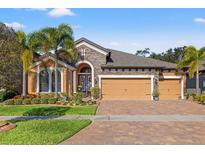 Charming single Gathering home with brick driveway, three-car garage, stone accents, and lush, tropical landscaping at 13711 Moonstone Canyon Dr, Riverview, FL 33579
