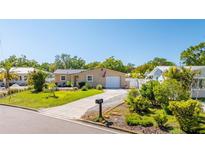 Charming single-story home with a well-manicured lawn, lush landscaping, and a paved driveway leading to an attached garage at 2016 Culberson Ave, Dunedin, FL 34698