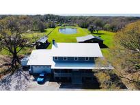 Stunning aerial view of home with metal roof, garage, and picturesque pond on expansive green property at 7705 W Four Pines Rd, Plant City, FL 33565