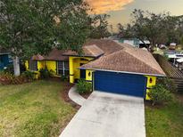 Eye-level view of a vibrant yellow single-story home with a blue two-car garage and well-maintained lawn at 1875 Oak Branch Dr, Sarasota, FL 34232