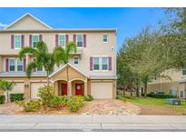 Charming townhouse with a brick driveway, red door, garage, and a manicured, landscaped yard with tropical plants at 876 Callista Cay Loop, Tarpon Springs, FL 34689