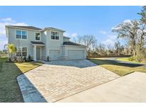 Two-story home featuring a brick driveway, two-car garage, manicured lawn, and modern architectural design at 22990 Scaglione Dr, Lutz, FL 33549