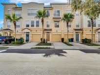 View of a three-story townhouse with a tan exterior, complemented by palm trees and individual garages at 3106 Bayshore Oaks Dr, Tampa, FL 33611