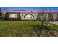 Unique home exterior with stone accents, an arched gated entryway, and lush green lawn at sunset at 3248 Rock Valley Dr, Holiday, FL 34691