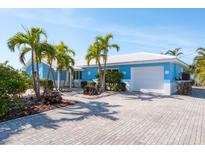 Charming blue single-story home featuring a white roof, palm trees, and a brick driveway at 4550 Plaza Way, St Pete Beach, FL 33706