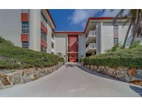 Beautiful condo building with white walls, red trim, nicely manicured hedges, and a walkway leading to a red front door at 2612 Pearce Dr # 310, Clearwater, FL 33764
