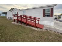 Ramped entrance of a single-story mobile home featuring red trim and neutral siding at 222 N Saint George Cir, Apollo Beach, FL 33572