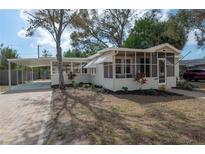 Quaint home with a screened porch and carport, complemented by a brick driveway and lush landscaping at 560 80Th N Ave, St Petersburg, FL 33702
