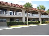Two-story condo featuring a red tile roof, second story balconies, and manicured landscaping at 1750 Belleair Forest Dr # A7, Belleair, FL 33756