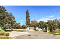 A sunny street view of a property with a gate in front and a very tall tree in the landscape at 7124 Jasmin Dr, New Port Richey, FL 34652