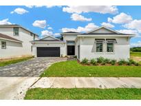 Beautiful single-story home with a well-manicured lawn, a paver driveway, and a modern black garage door at 10432 Torchwood Sea Way, San Antonio, FL 33576