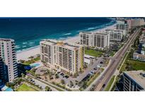 Stunning aerial view of beachfront condos with a pool, lush landscaping, and pristine sandy beach on a sunny day at 1480 Gulf Blvd # 410, Clearwater Beach, FL 33767