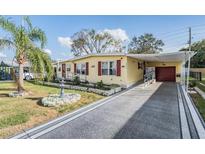 Charming yellow home featuring a covered driveway, red shutters and manicured lawn with a fountain at 36936 Kay Ave, Zephyrhills, FL 33542