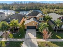 An aerial view of a tan two-story home with a black roof, attached garage and lake views at 11720 Winterset Cove Dr, Riverview, FL 33579