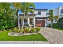 Inviting two-story home with a brick driveway, a well-kept lawn, palm trees and a cozy porch at 47 Adalia Ave, Tampa, FL 33606