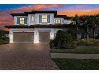 Elegant two-story home featuring a brick driveway, two-car garage, and lush landscaping during a beautiful sunset at 28565 Picana Ln, Wesley Chapel, FL 33543