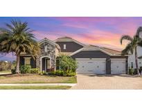 Stunning home featuring a stone facade, paver driveway, tropical landscaping, and a three-car garage at 11930 Perennial Pl, Bradenton, FL 34211