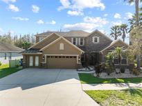 View of the exterior of a tan two story home, with well manicured lawn, three car garage and mature trees at 19238 Climbing Aster Dr, Tampa, FL 33647