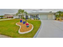 Well-manicured lawn features unique planters in front of this bright home with attached garage and mature landscaping at 1805 Columbine Pl, Sun City Center, FL 33573