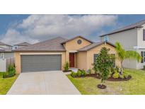 Tan single-Gathering home featuring a two-car garage, neutral landscaping, and a well-manicured lawn at 9313 Channing Hill Dr, Ruskin, FL 33573