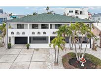 Elegant two-story home featuring a green roof, white exterior and beautiful landscaping with mature palms at 2710 Hibiscus W Dr, Belleair Beach, FL 33786