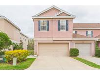 Two-story pink home with a two-car garage, black shutters, and well-maintained landscaping at 10011 Tranquility Way, Tampa, FL 33625