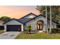 Charming single-story home featuring a well-manicured lawn, arched entryway, and a two-car garage, all beneath a picturesque sunset at 15004 Elmcrest St, Odessa, FL 33556