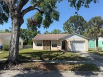 Charming single-Gathering home with a well-maintained lawn, featuring a beige exterior, an attached garage, and a stone column at 7425 Riverbank Dr, New Port Richey, FL 34655