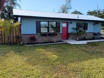 Charming home with a well-maintained lawn, garden beds, and a bright red front door at 402 Mary St, Punta Gorda, FL 33950