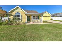 Charming yellow home with green door, front porch, and well-manicured lawn at 6217 Evansbrook Dr, Zephyrhills, FL 33541