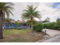 Charming blue single-story home featuring mature palm trees, a lush lawn, and a cozy porch swing for relaxed outdoor living at 10754 111Th N Pl, Largo, FL 33778