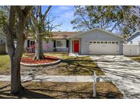 Charming home featuring a red front door, lush landscaping, and a well-maintained lawn at 1582 Sandalwood Dr, Dunedin, FL 34698