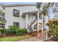 Two-story condo with white exterior, wooden stairs, and charming curb appeal from flower pots and green bushes at 1822 Lake Cypress Dr # 1822, Safety Harbor, FL 34695