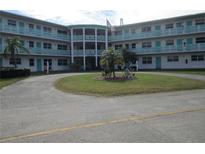Low-angle exterior of a condominium building with a circle driveway, lawn, and U.S. flag at 1950 59Th N Ave # 212, St Petersburg, FL 33714