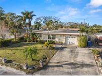 Charming single-story home with a well-manicured lawn, mature palm trees, and a driveway leading to an attached garage at 1015 55Th S Ave, St Petersburg, FL 33705