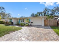 Charming single-story home with a well-maintained front yard, patterned brick driveway and vibrant blue accents at 1095 Jackmar Rd, Dunedin, FL 34698