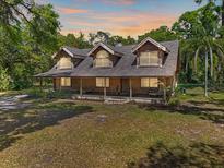 Charming two-story log home featuring a welcoming front porch and mature trees under a beautiful colorful sky at 14206 Walden Sheffield Rd, Dover, FL 33527