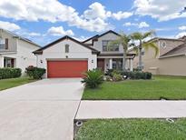 Charming two-story home with well-manicured lawn, beautiful landscaping and a red two car garage door at 4136 Shrewbury Pl, Land O Lakes, FL 34638