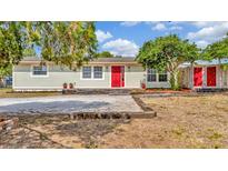 Charming single-story home with light siding, red door, mature trees and welcoming curb appeal at 7421 Andre Dr, Zephyrhills, FL 33541