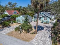 Charming light blue home featuring a brick driveway, lush landscaping, and a detached garage at 410 Georgia Ave, Crystal Beach, FL 34681