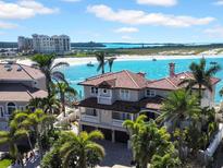 Beautiful waterfront home featuring a tile roof, balcony, mature landscaping, and beachfront access to white sand and turquoise waters at 940 Monte Cristo Blvd, Tierra Verde, FL 33715