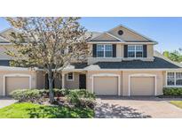 A tan two-story townhouse featuring a paved driveway, beige garage doors, and manicured landscaping at 26900 Juniper Bay Dr, Wesley Chapel, FL 33544