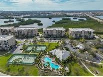 Aerial view of the community featuring tennis courts, a pool, and buildings surrounded by lush greenery and water views at 7194 Key Haven Rd # 405, Seminole, FL 33777