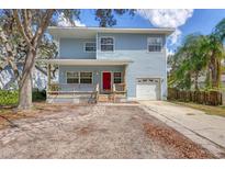 Charming two-story home with light blue siding, red door, a front porch and attached garage at 12227 Noreast Lake Dr, Tampa, FL 33612