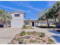 Two-story home featuring white walls, desert landscaping and palm trees against a blue sky at 590 Baywood N Dr, Dunedin, FL 34698