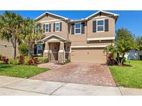 Charming two-story home showcasing a manicured lawn, stone accents, and a brick driveway at 12225 Lake Blvd, New Port Richey, FL 34655